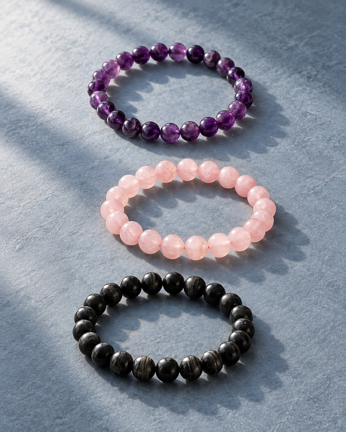Amethyst, rose quartz and black tourmaline bracelets on grey stone