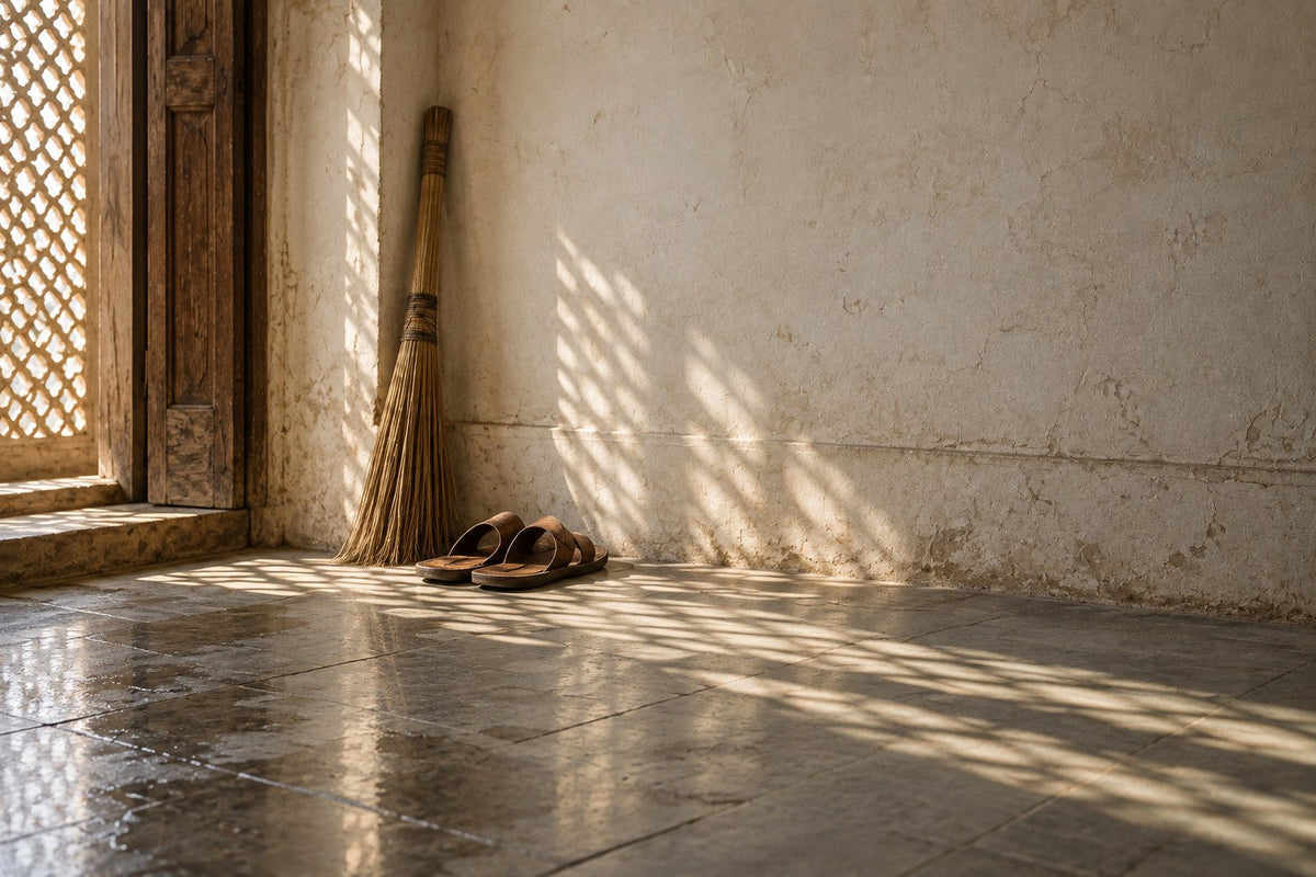 Chappals and a broom by a freshly washed stone floor in jaali light