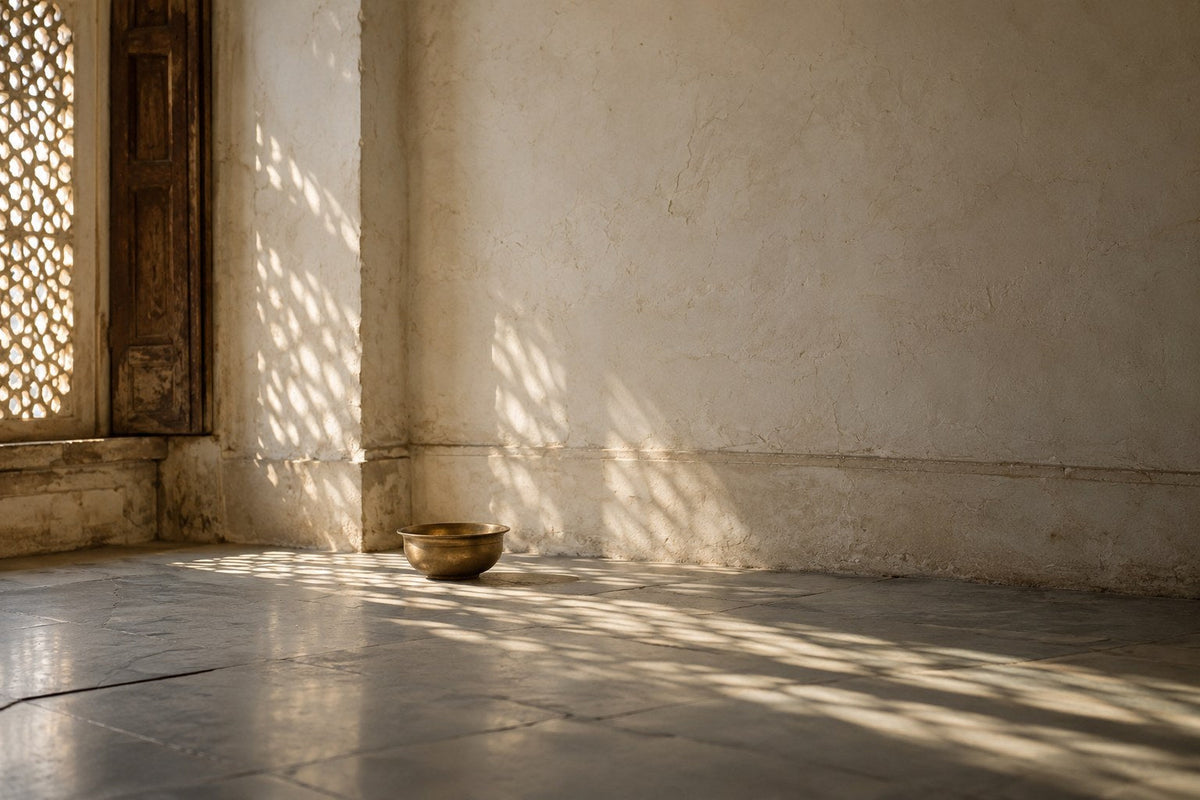 Morning light through a carved sandstone jaali across an empty room with a brass bowl