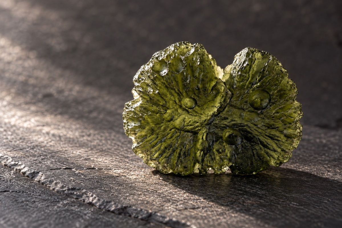Two pieces of green moldavite on dark slate in raking light