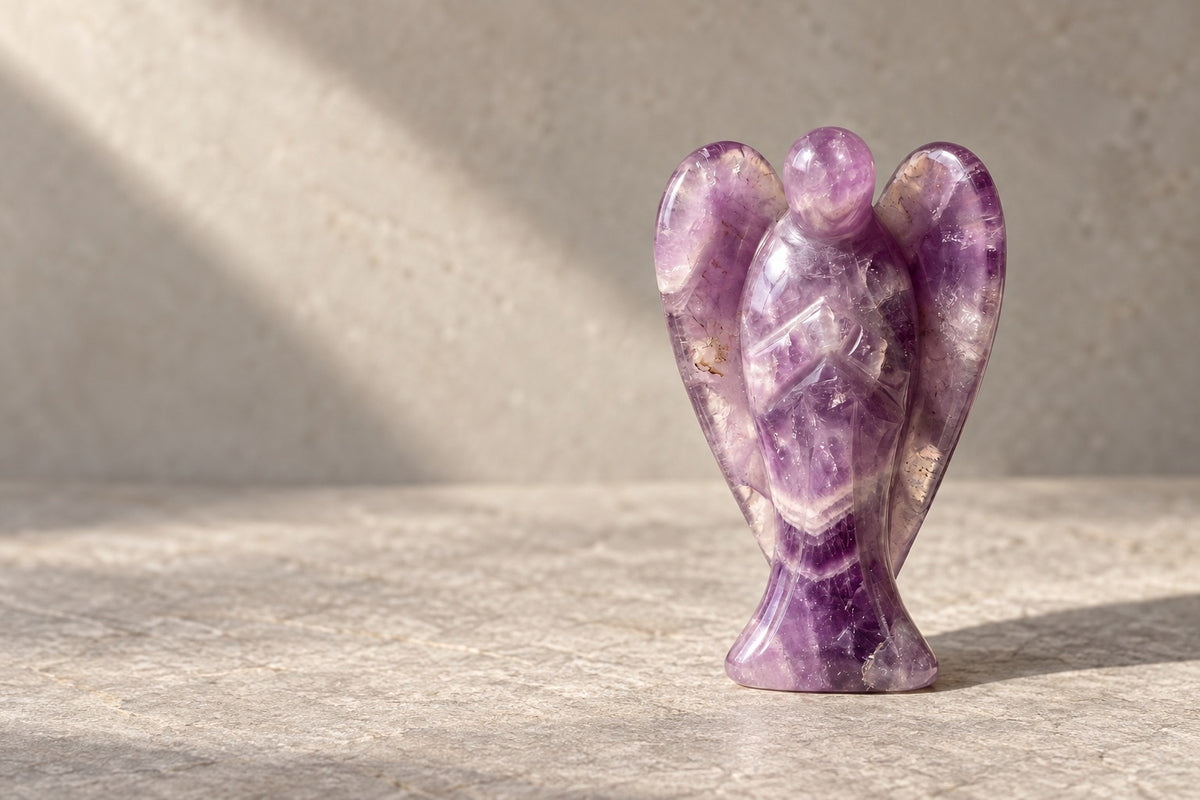 Carved amethyst angel standing on pale stone in soft sunlight