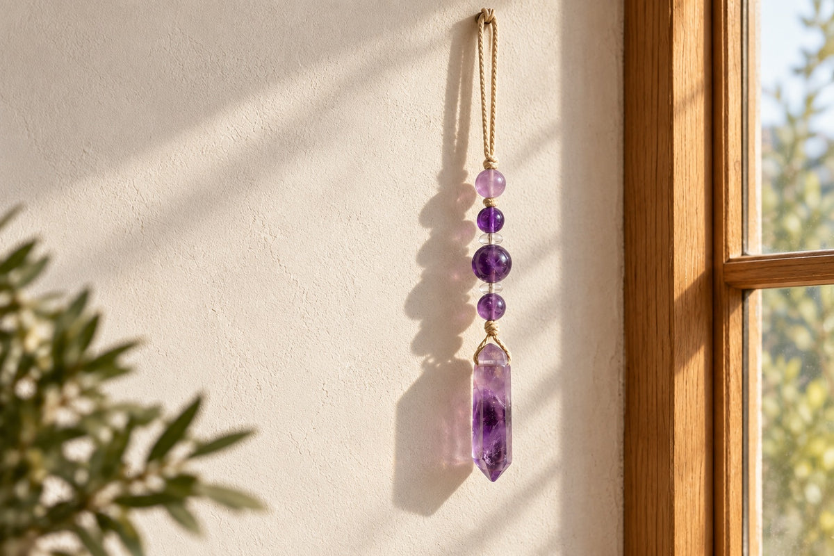 Amethyst bead and point hanging against a pale wall by a window