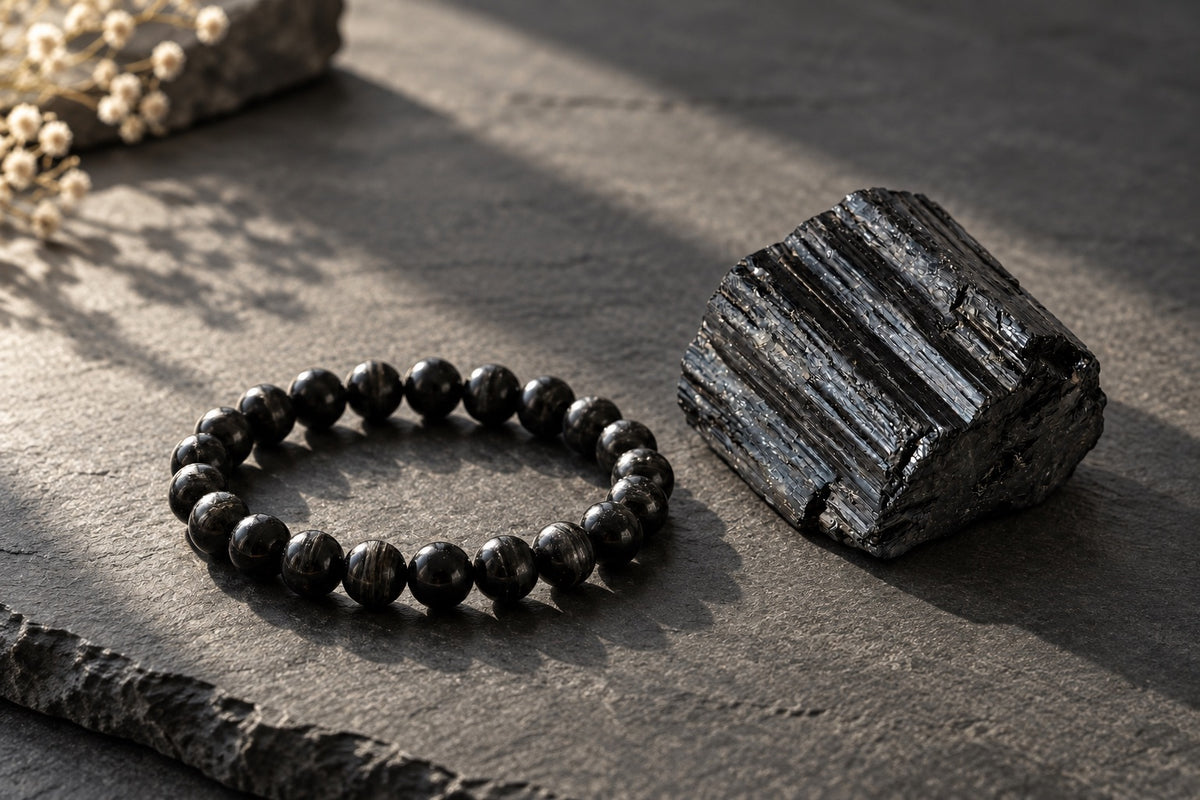 Black tourmaline bracelet beside a raw black tourmaline stone on slate