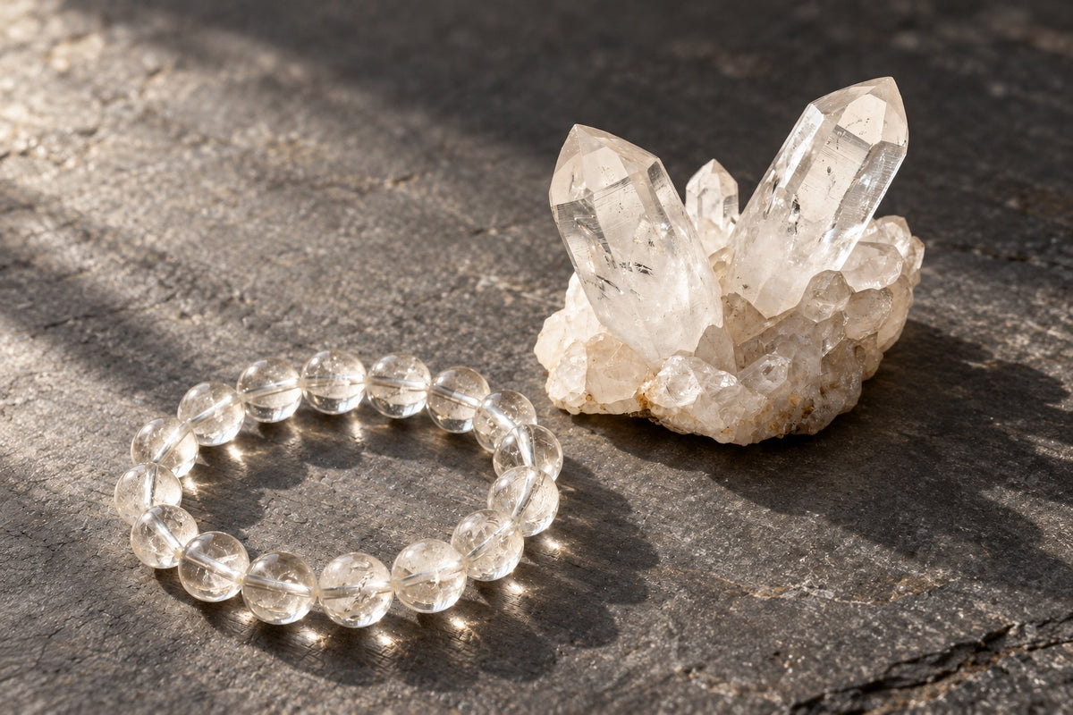 Clear quartz bracelet beside a raw clear quartz cluster on dark slate