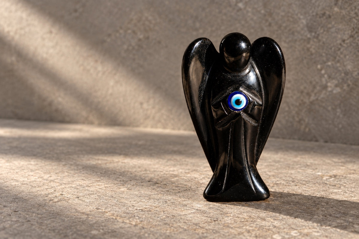 Black stone angel with an evil eye charm on pale stone