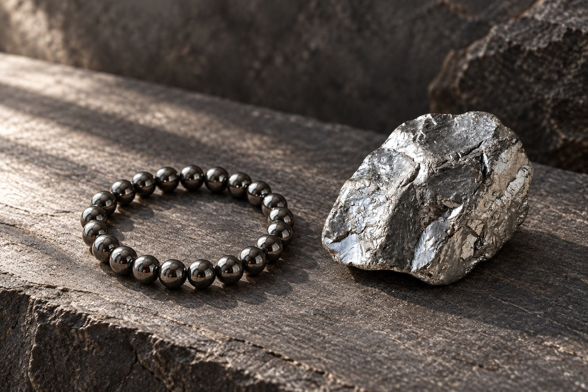 Hematite bracelet beside a raw hematite stone on dark slate