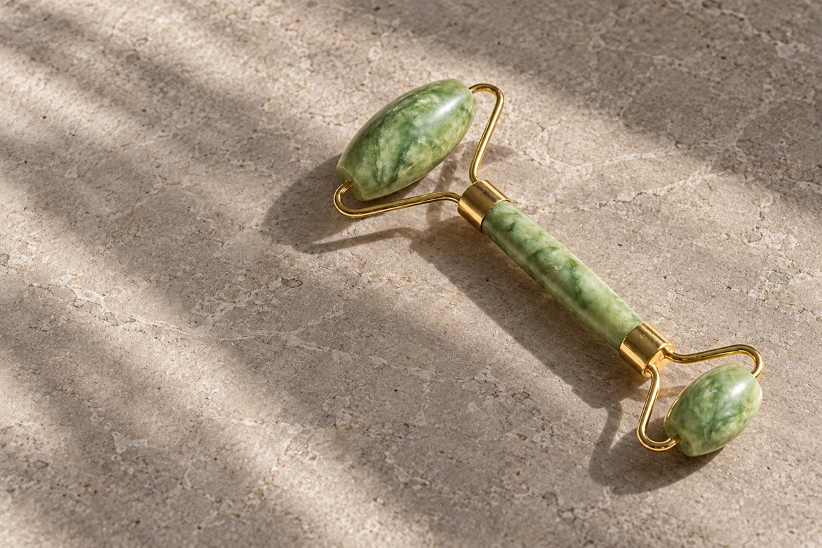 Green jade face roller with gold fittings on pale stone