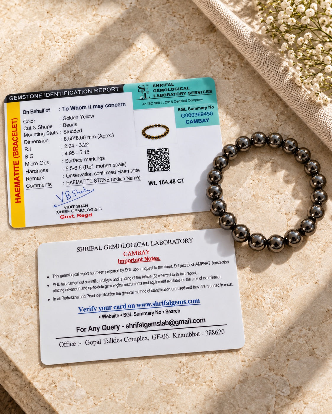 Rapporto di identificazione gemmologica di un laboratorio gemmologico, fronte e retro, che identifica un bracciale in ematite, accanto a un bracciale di perle di ematite