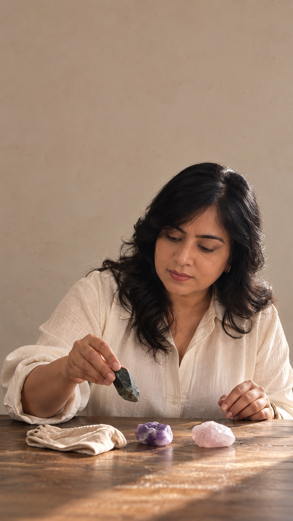 Lavina Jhalani at a wooden table choosing crystals, holding a small dark stone